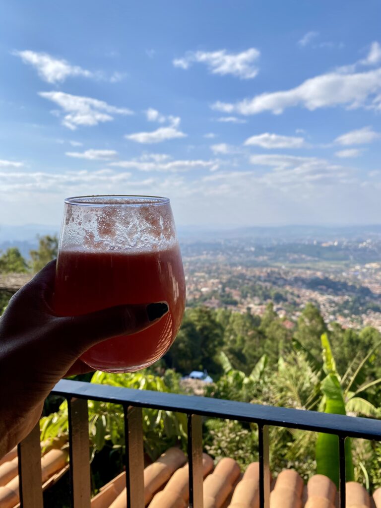 a glass of watermelon juice held up against the backdrop of kigali views