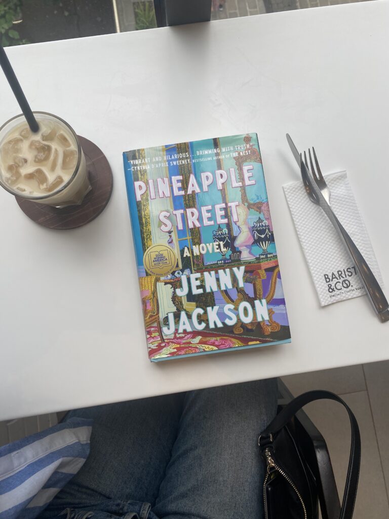the book pineapple street lays next to an ice latte 