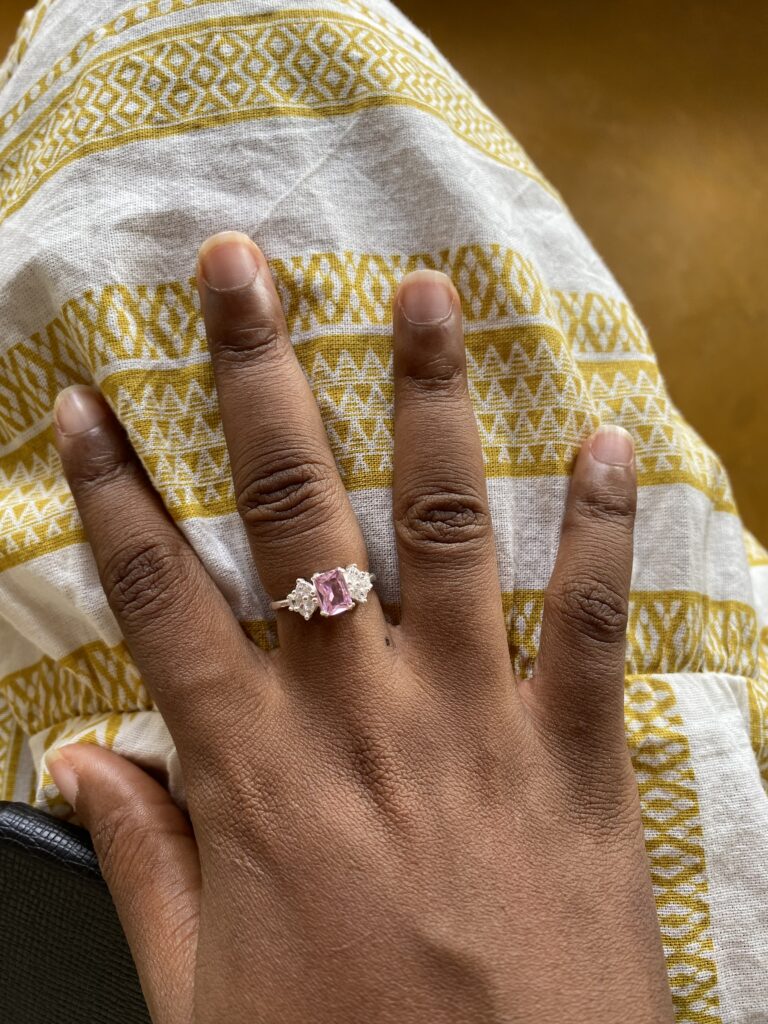 a black woman's hand wearing a silver ring with a pinks tone
